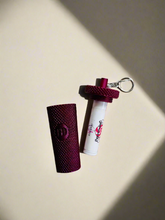 Load image into Gallery viewer, Maroon textured case and white cylindrical item with red design on a beige carpet
